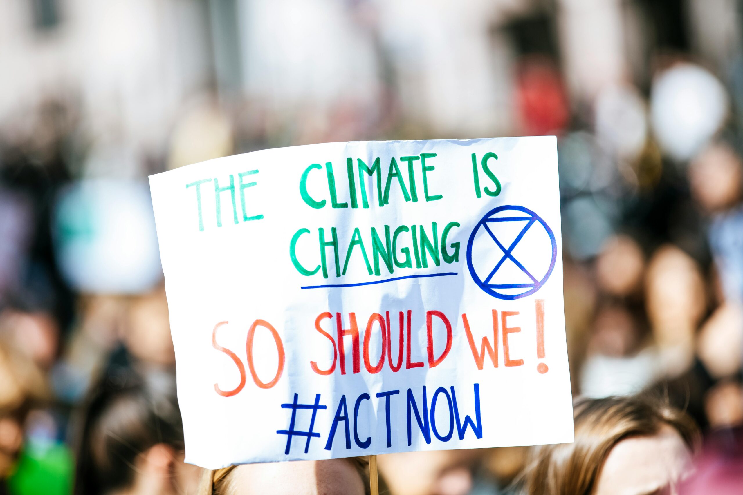 Crowd gathering for climate change protest, holding activist sign.